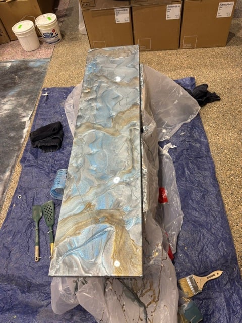 Marble countertop sample wrapped in plastic on blue tarp in work area with cardboard boxes and supplies