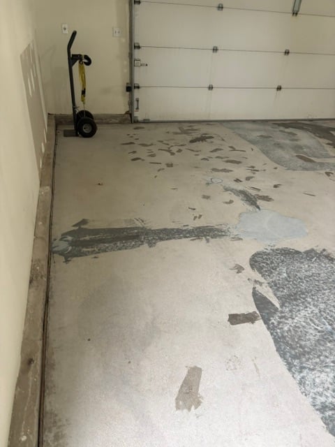 Garage floor with partially removed epoxy coating exposing concrete underneath, electric scooter against wall, and white garage door