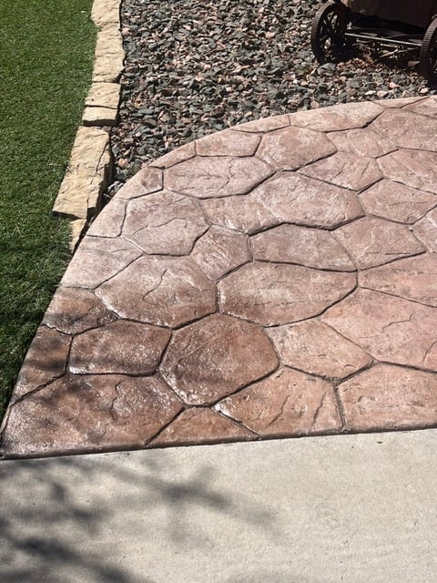 Stamped concrete patio with stone pattern next to green artificial turf and gravel driveway