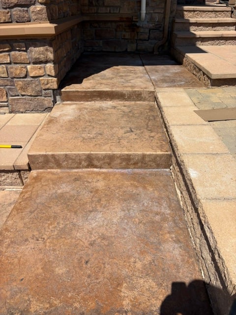 Stone walkway with stepped entrance, stone walls on sides, and brick structures in background under sunlight