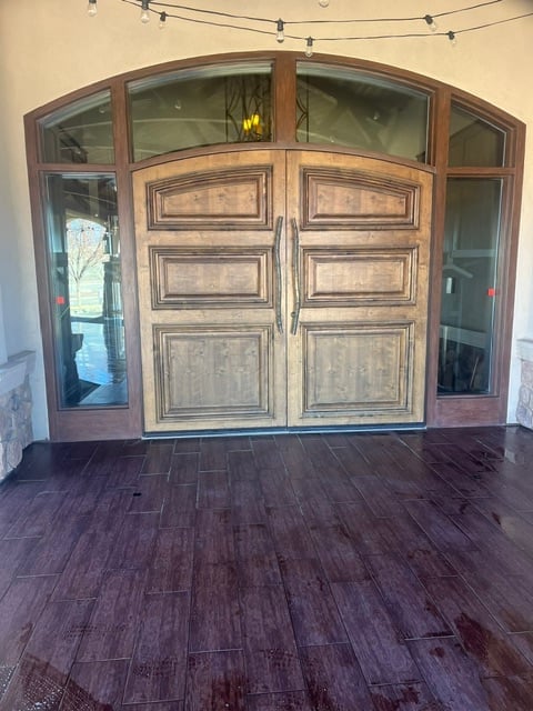 Large wooden arched entryway with dual doors and glass panels in an elegant interior foyer with dark hardwood flooring