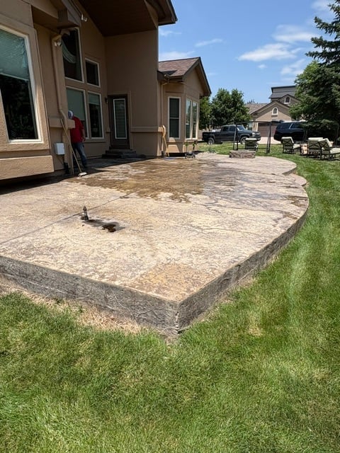 Concrete patio behind residential home with manicured lawn and neighboring houses visible in background