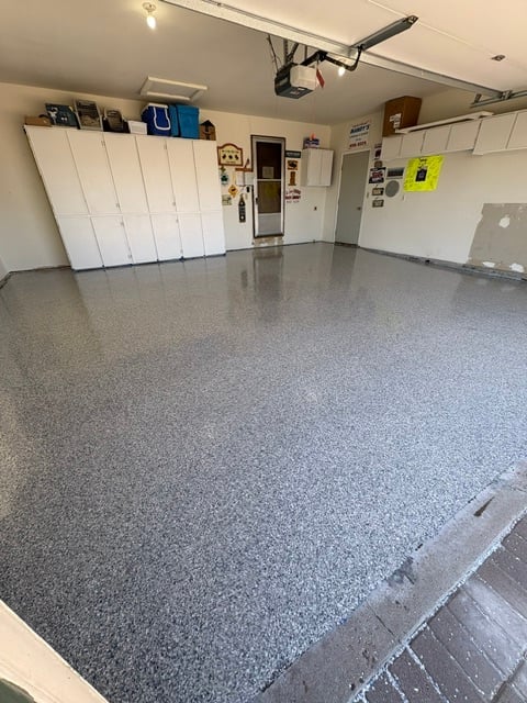 Clean garage interior with white cabinets, gray epoxy floor, overhead projector, and organized storage shelving