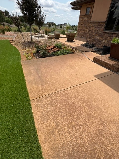 Modern backyard patio with concrete pavement, manicured lawn, landscaping beds, and brick home with scenic hillside view