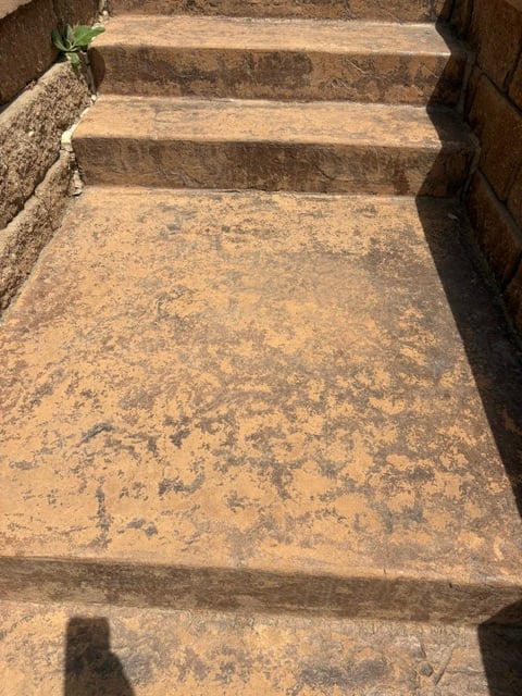 Outdoor stone steps with weathered tan and gray concrete, bordered by brown brick walls, descending into shadow