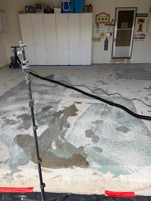 Garage floor with water damage and a wet-vac hose, white cabinets and storage visible in background