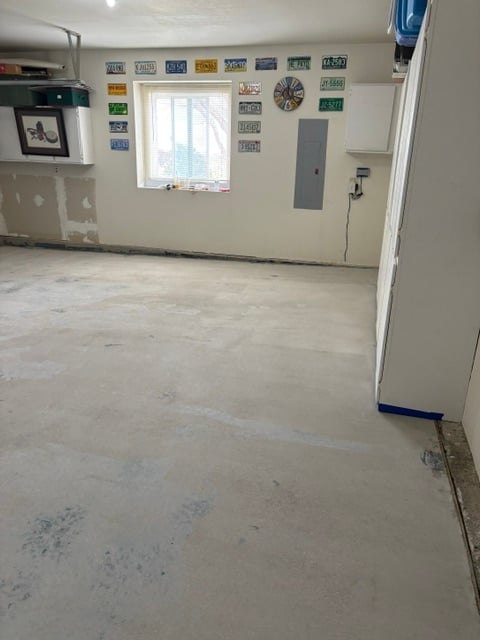 Empty garage interior under renovation with concrete floor, white walls, window, and vintage license plates displayed on wall