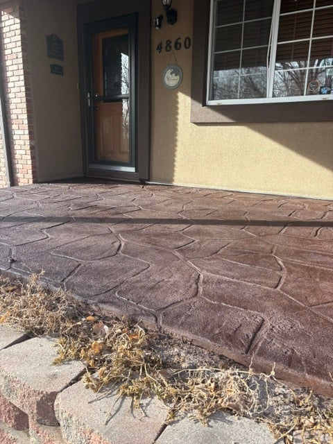 Front entrance of house number 4860 with brown patterned concrete patio, wooden door, and tumbleweeds on the ground