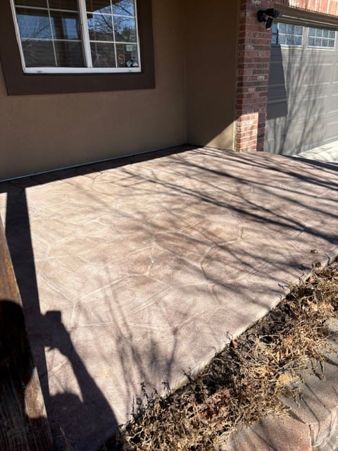 Concrete patio with tree shadows cast across it, attached to a tan and brick house with windows