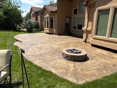 Large residential patio with fire pit, surrounded by manicured lawn and home exterior with stone foundation