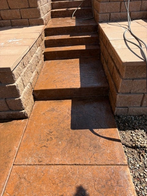 Outdoor brick staircase with rust-colored tiles and dark treads, flanked by brown brick walls and paved walkway