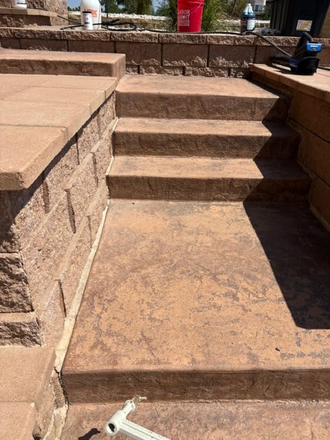 Outdoor concrete pathway with brown stone steps leading upward between retaining walls on a sunny day