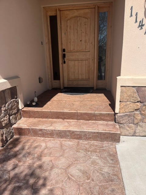 Front entrance with wooden door, sidelights, terracotta tile steps and flooring, and stone wall details on a sunny day